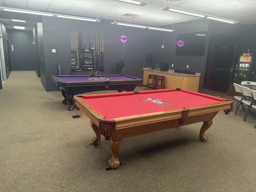 Two pool tables with neon signs and a cue rack
